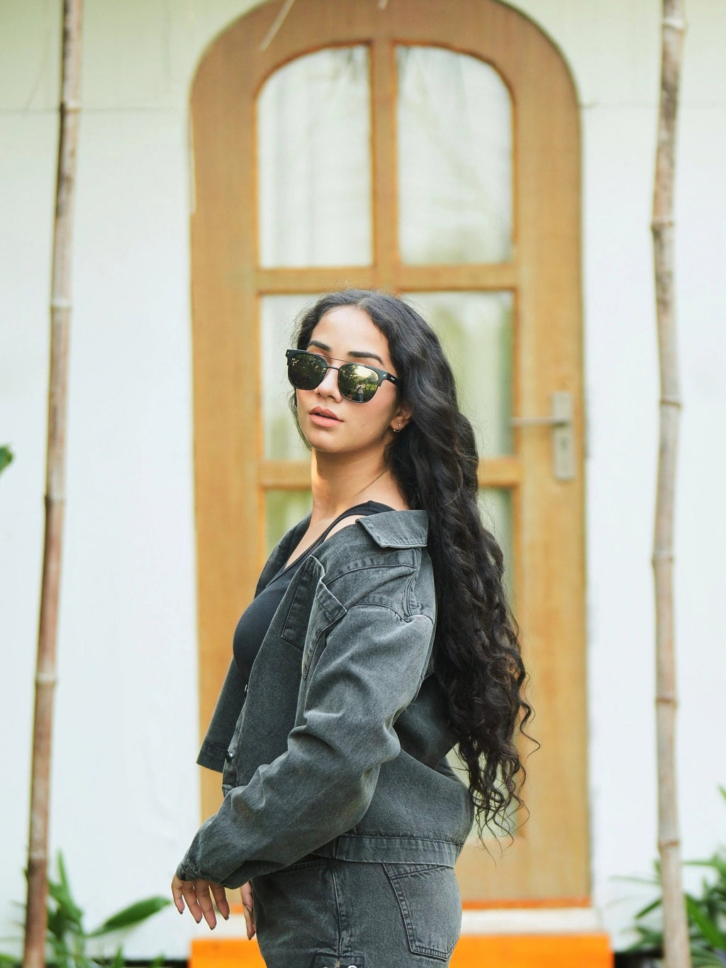 Woman wearing sunglasses and a denim jacket in front of a wooden door.