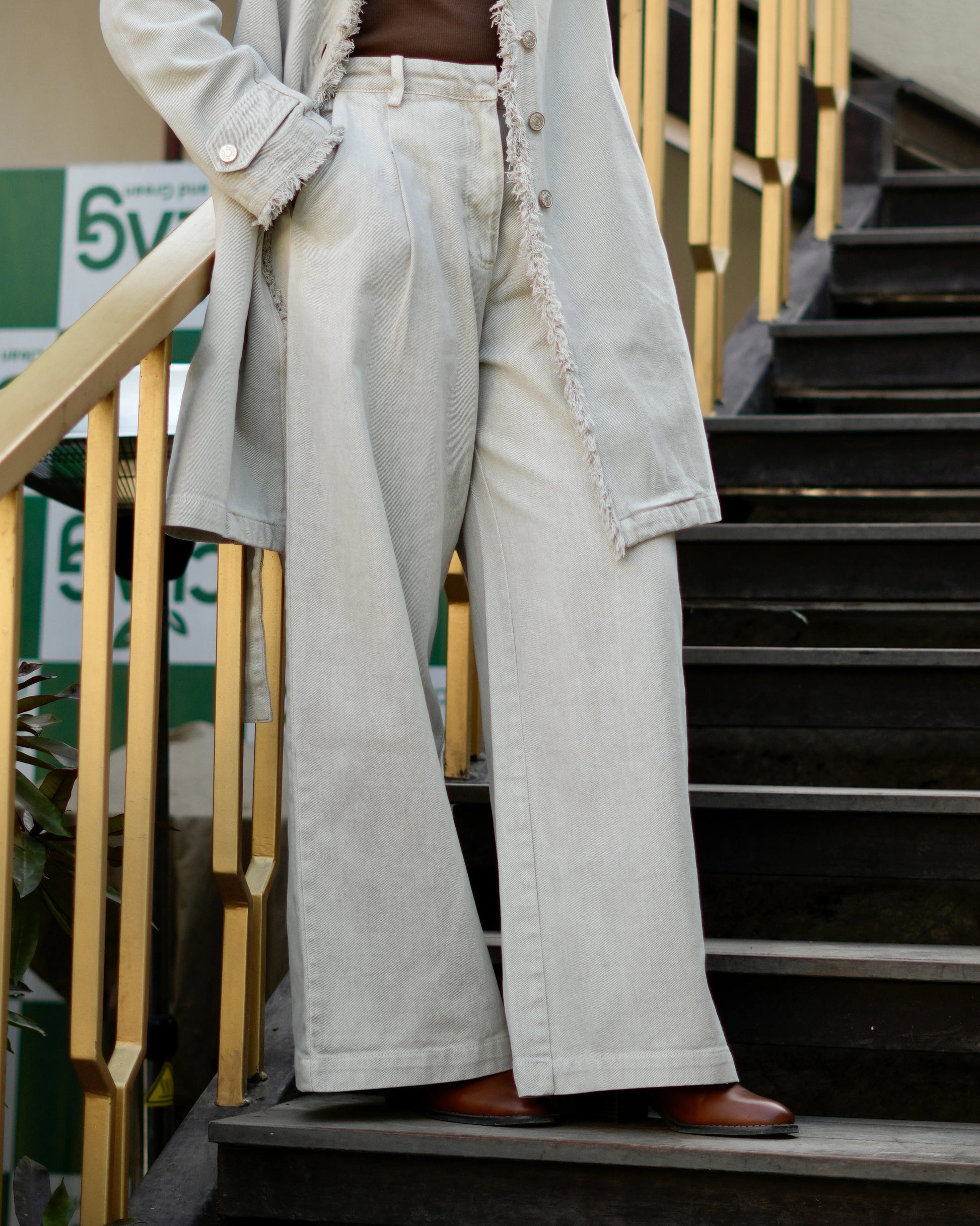 Woman in a beige coat and white pants standing on stairs outdoors