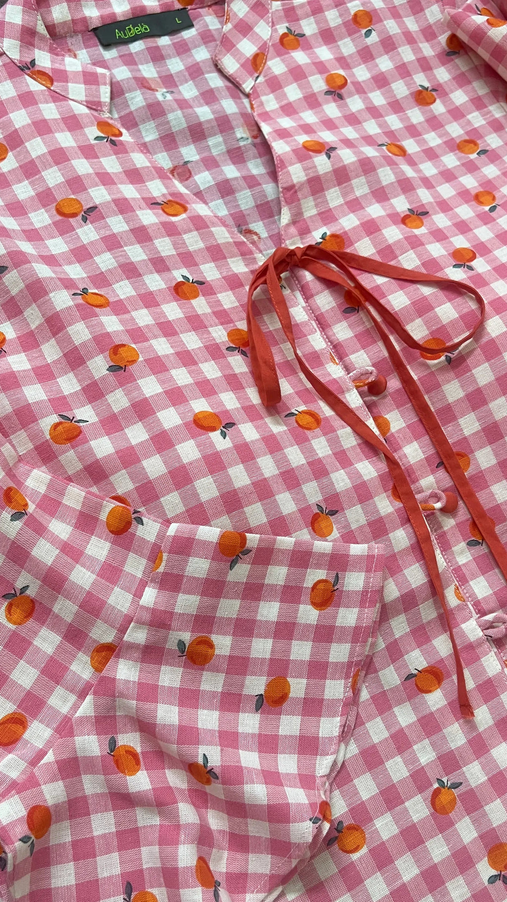 Pink checkered shirt with orange fruit pattern on a wooden surface