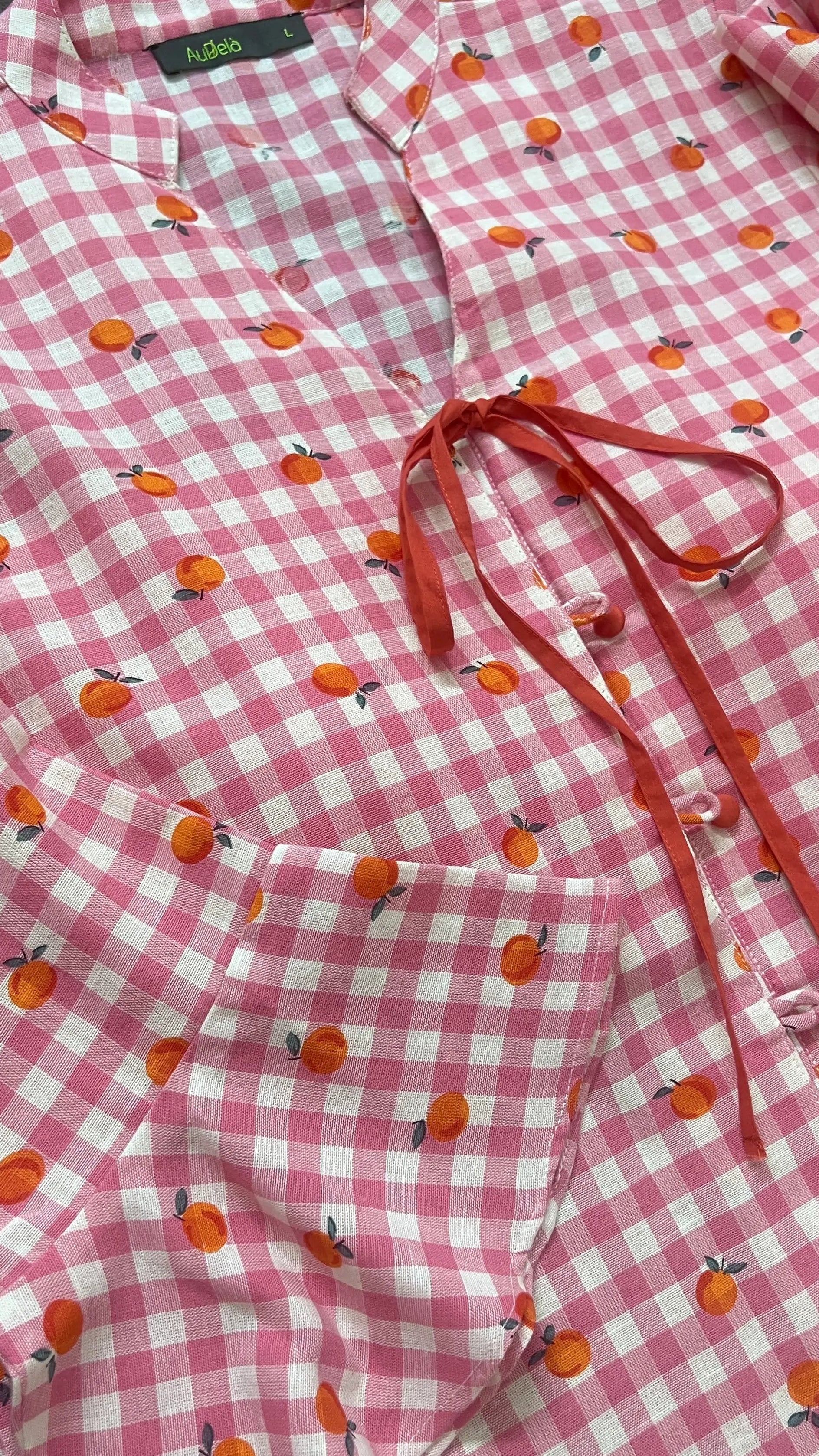 Pink checkered shirt with orange fruit pattern on a wooden surface