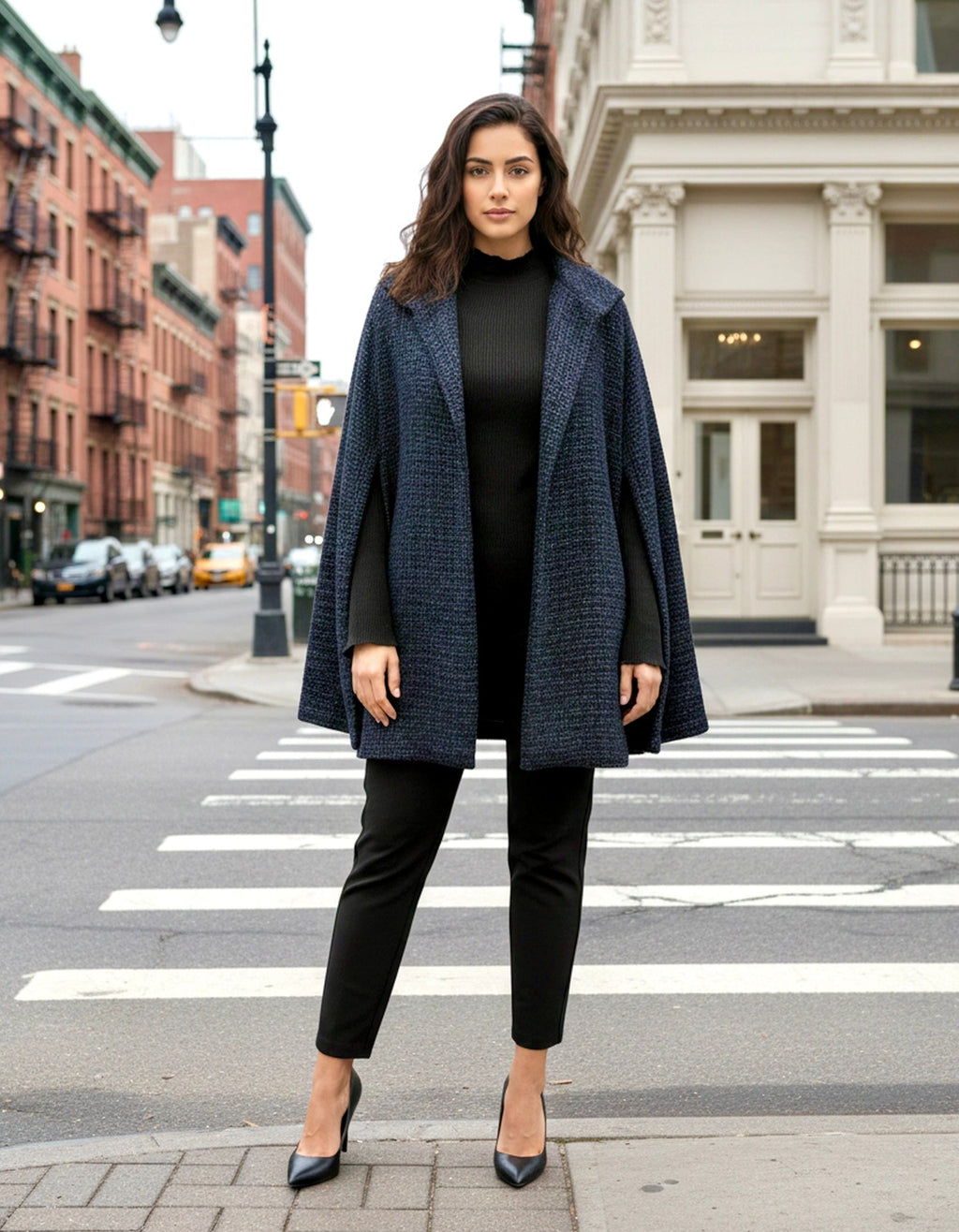 Woman in a blue open cape jacket standing on a city street