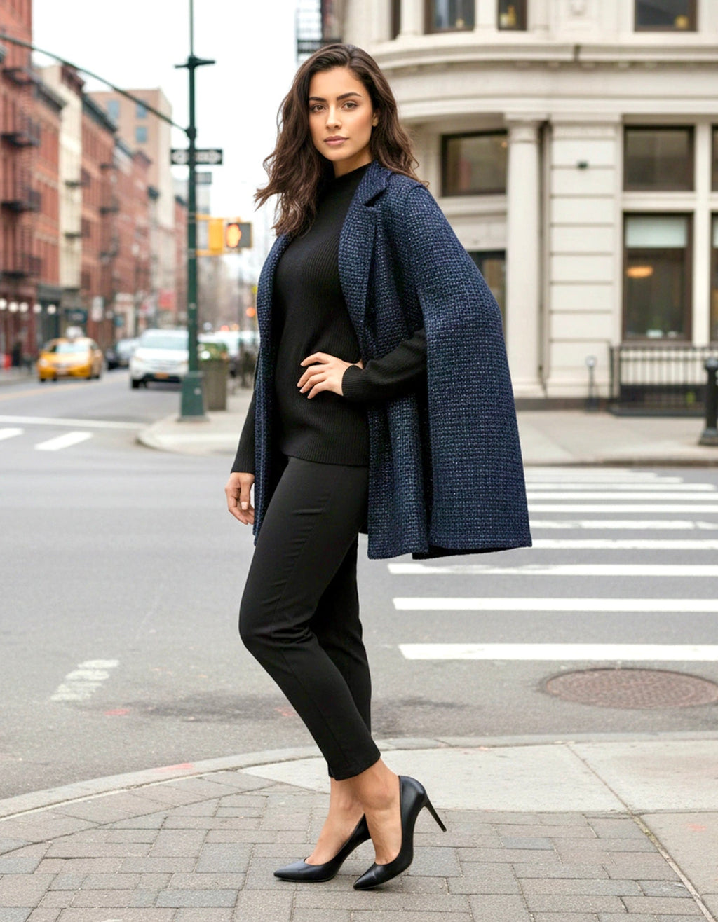 Woman in a black outfit with a blue coat standing on a city street.