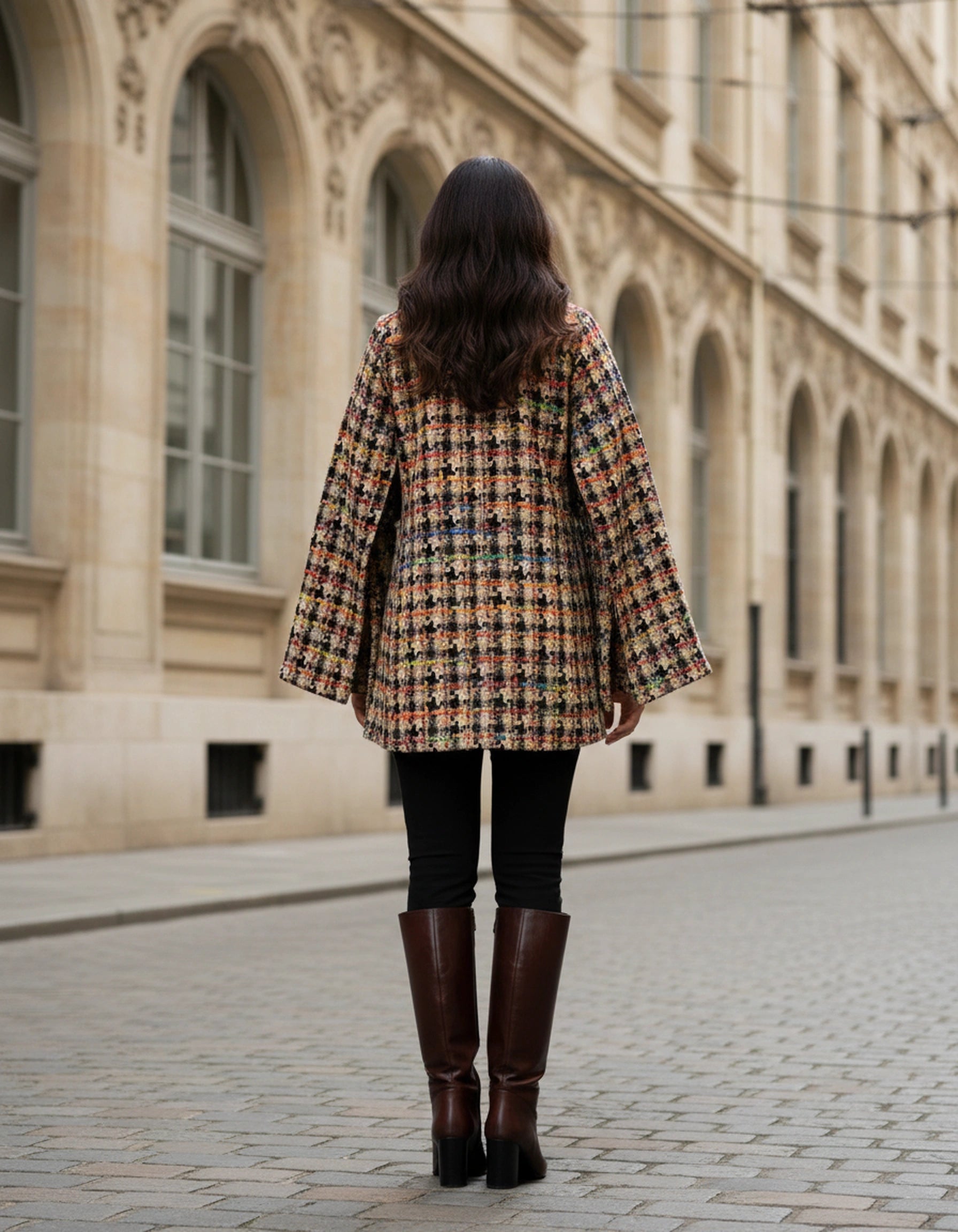 Person wearing a plaid coat and brown boots walking away from a building with arched windows.